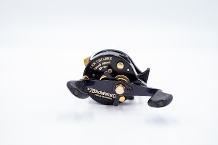 A fishing reel, specifically a Lew Childre Speed Spool model, is prominently displayed against a plain white background. The reel is predominantly black with metallic gold details, featuring the brand name 'Browning' and mentioning '3 ball bearings' in gold lettering. The handles are textured for grip, and the design suggests durability and precision, typical of a high-quality fishing reel.
