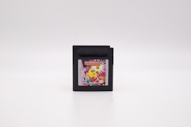 A black cartridge with a colorful label featuring a yellow character and bright design elements, set against a plain white background.