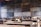 A classroom setting features several old-fashioned sewing machines on wooden desks lined in rows. The background includes a wall of chalkboards covered with writing, creating an atmosphere of a vintage educational or vocational training environment.