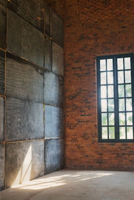 An empty room with brick walls and a large window letting in sunlight. One wall is covered with multiple chalkboards filled with handwritten calculations and notes.