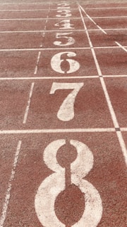 A close-up view of a running track with numbered lanes, specifically lanes 3 through 8,. The track surface is reddish-brown with white lines and numbers indicating each lane.