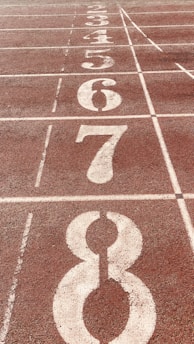 A close-up view of a running track with numbered lanes, specifically lanes 3 through 8,. The track surface is reddish-brown with white lines and numbers indicating each lane.