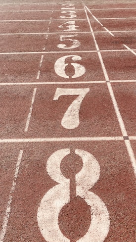 A close-up view of a running track with numbered lanes, specifically lanes 3 through 8,. The track surface is reddish-brown with white lines and numbers indicating each lane.