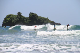 Surfers catching a clean wave at 'El Derechón' with the rugged coastline of Lobos Island in the background.