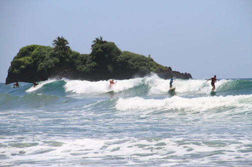 Surfers catching a clean wave at 'El Derechón' with the rugged coastline of Lobos Island in the background.