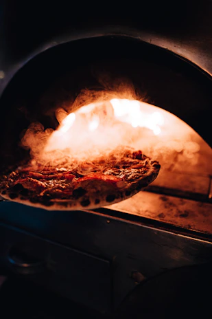 A chef expertly sliding a pizza into a traditional stone oven, flames glowing in the background.