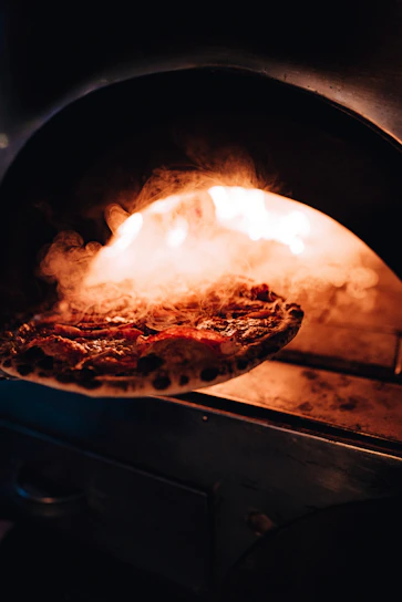 Warm close-up of a golden, bubbling pizza fresh out of a wood-fired oven.