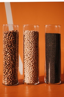 a row of three glass vases filled with grains