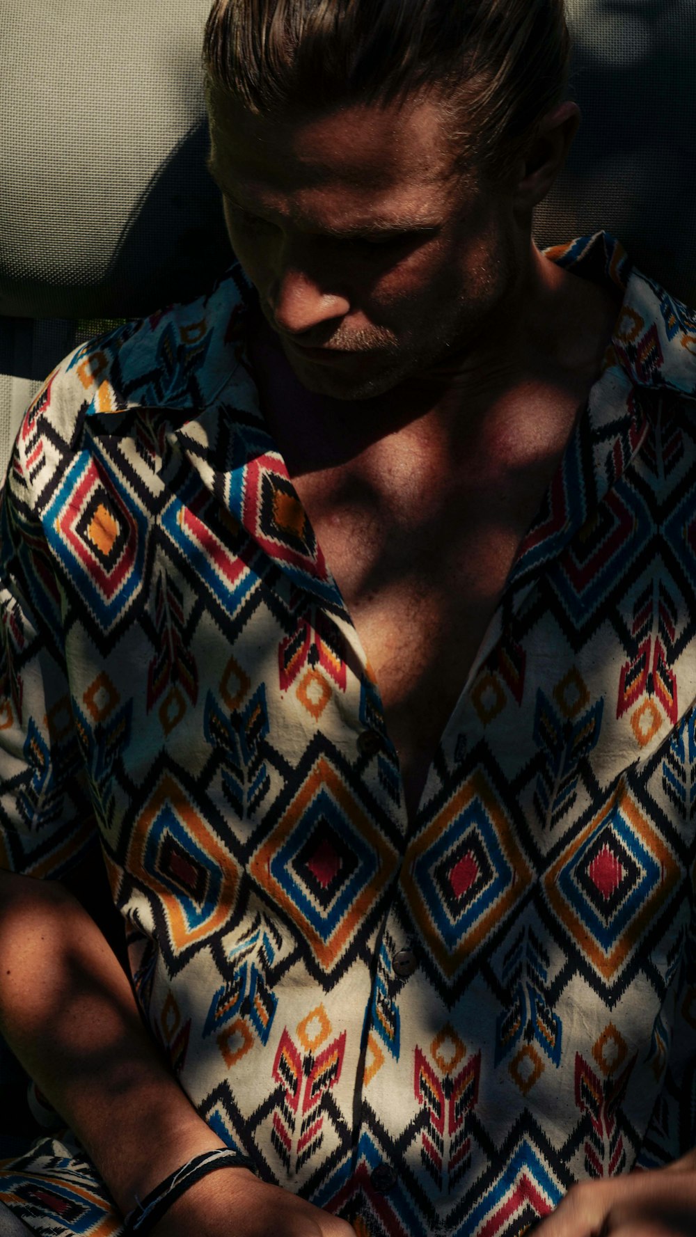 a man in a patterned shirt looking down at his cell phone