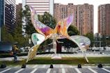 a sculpture in the middle of a park with buildings in the background