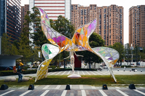 a sculpture in the middle of a park with buildings in the background