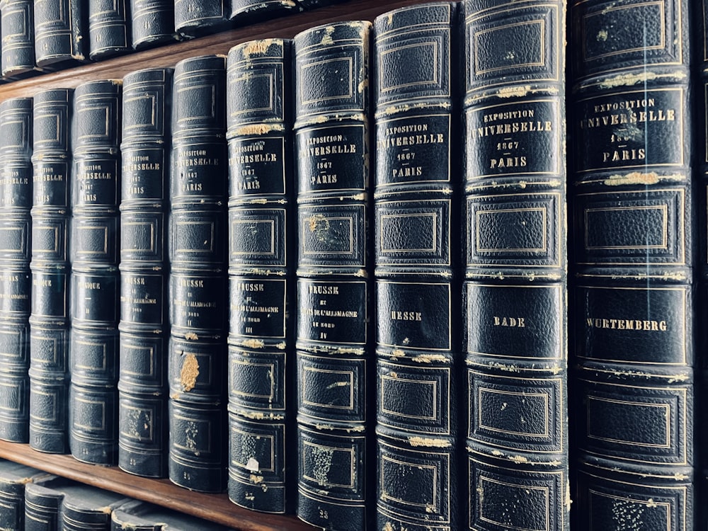 a row of black books sitting on top of a wooden shelf