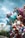 A cluster of colorful helium balloons, featuring various cartoon characters and shapes, including a unicorn, several animals, and a princess. The balloons are gathered together against an outdoor background, which includes part of a bridge and an overcast sky.