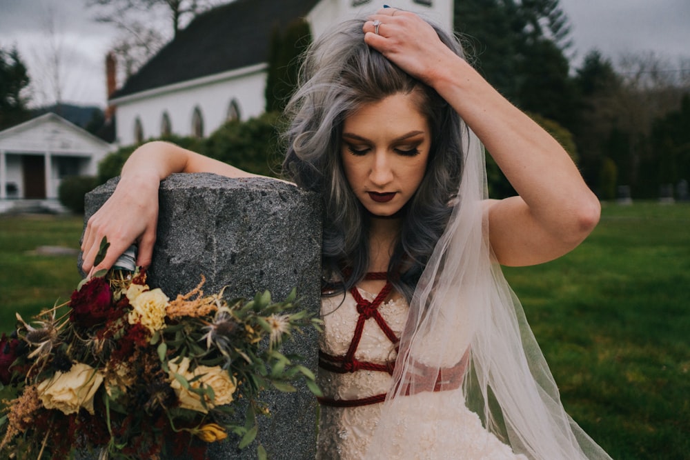 a woman in a wedding dress leaning on a rock