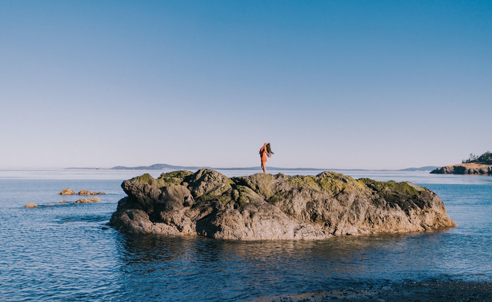 a person standing on a rock in the middle of the ocean