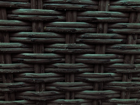 A close-up view of a woven pattern with a textured, grid-like structure. The material appears to be a dark, possibly synthetic fiber that crisscrosses to form a rigid surface. Each strand has a slightly glossy finish, adding depth and dimension to the pattern.