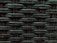 A close-up view of a woven pattern with a textured, grid-like structure. The material appears to be a dark, possibly synthetic fiber that crisscrosses to form a rigid surface. Each strand has a slightly glossy finish, adding depth and dimension to the pattern.