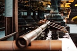 A traditional Japanese water basin with long wooden ladles placed across the edge. The background consists of blurred architectural and natural elements, suggesting a serene and historic setting.