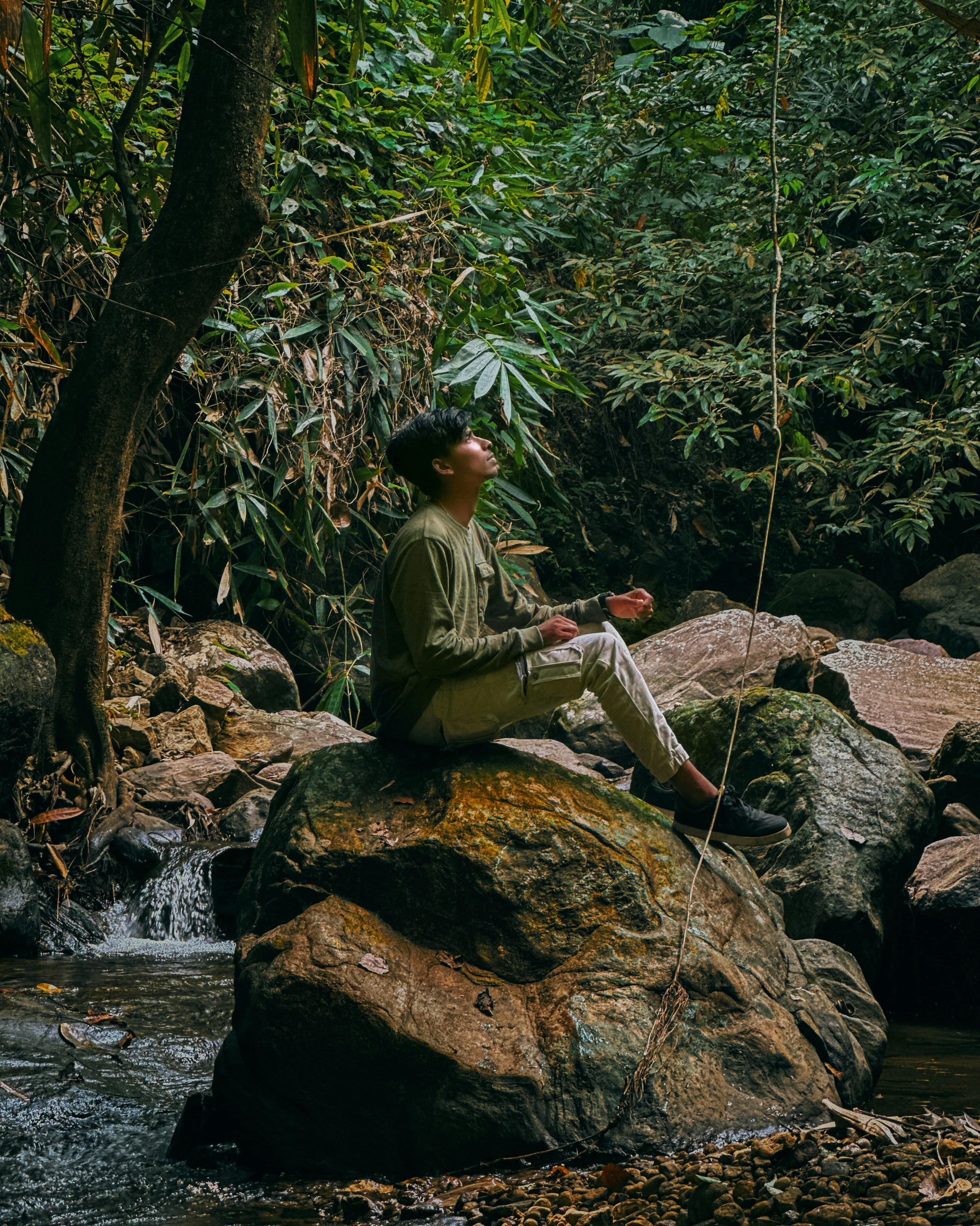 a man sitting on top of a rock next to a river