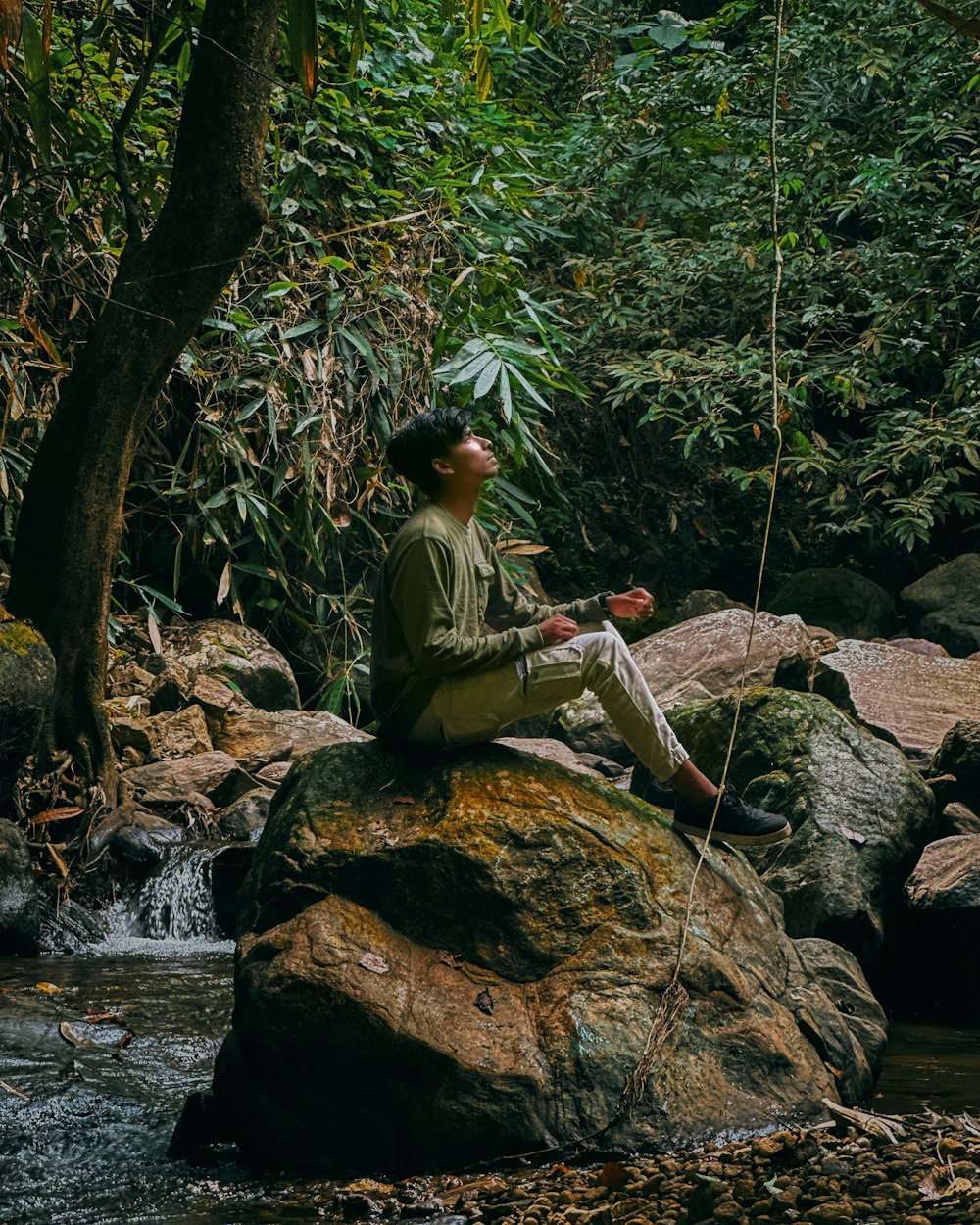 a man sitting on top of a rock next to a river