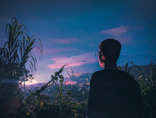 A person holding Glovibs glasses up against a city skyline at dusk, the lights twinkling in sync.