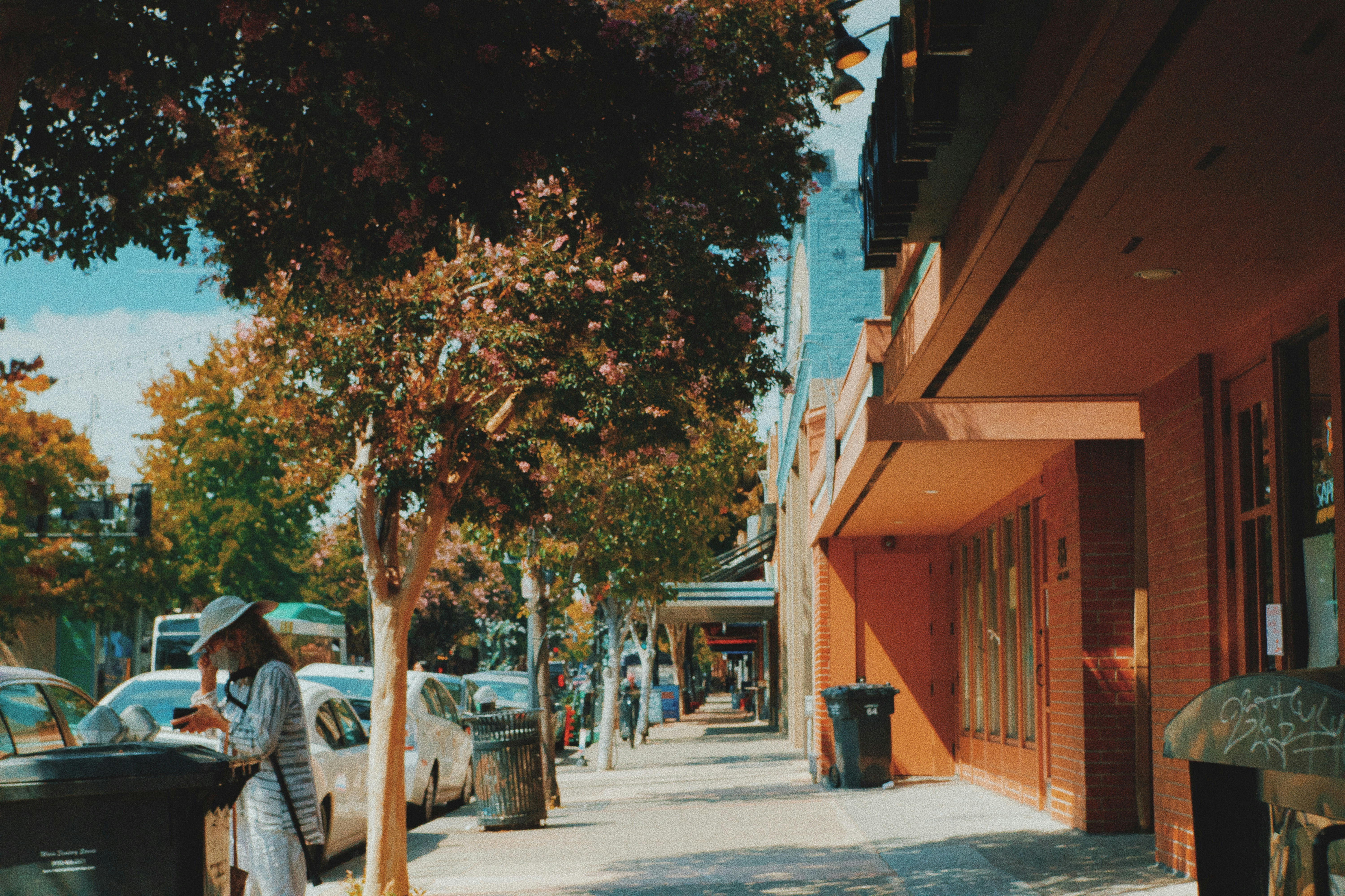 a woman walking down a sidewalk next to a tree