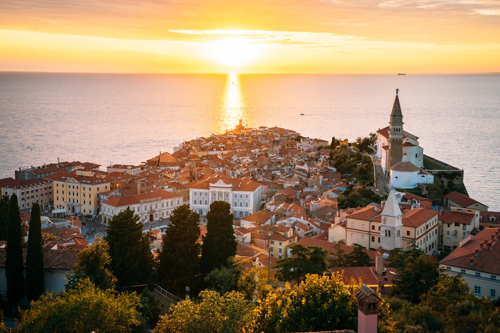 the sun is setting over a city by the ocean