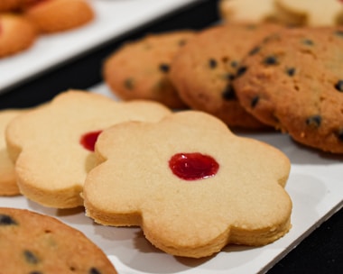 A close-up view of a selection of cookies placed on a white surface. There are flower-shaped cookies with a red center alongside round cookies with chocolate chips.