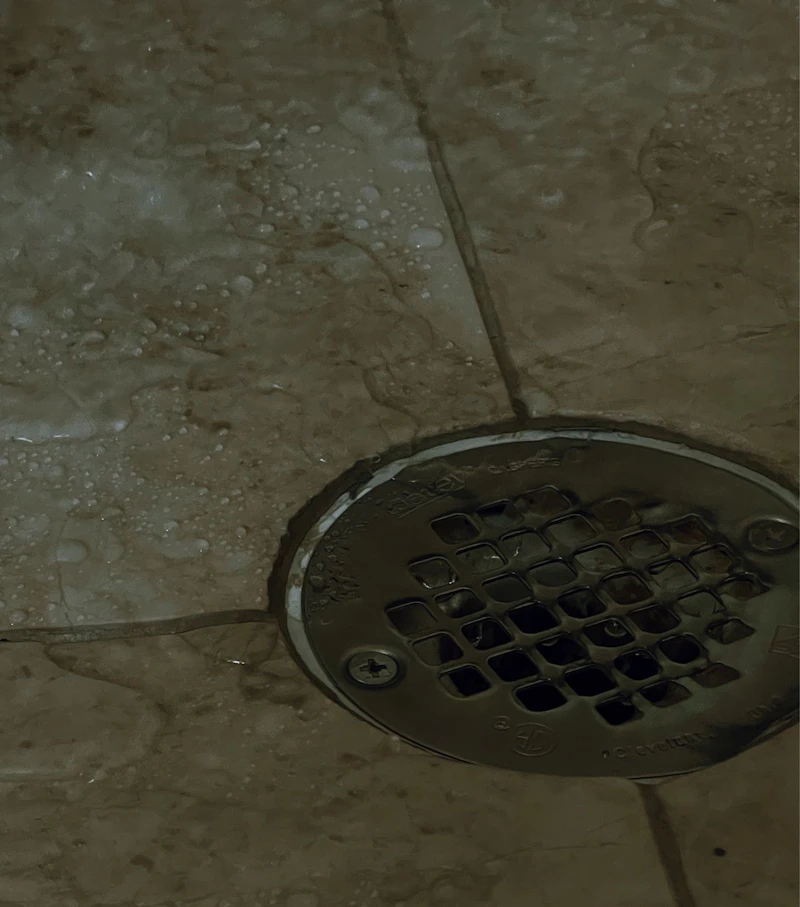 A round metal floor drain in a wet tiled floor