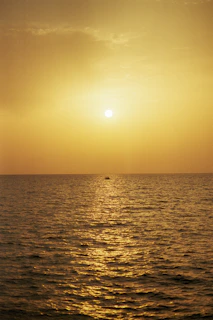A serene golden sunset over a calm ocean, with a silhouette of a small boat gently floating.