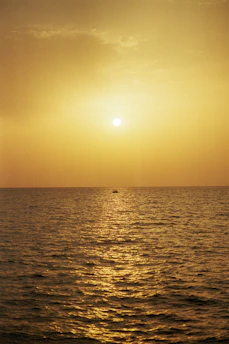 A serene golden sunset over a calm ocean, with a silhouette of a small boat gently floating.