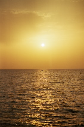 A serene sunset over a golden beach with a couple enjoying a private boat ride on calm ocean waters.