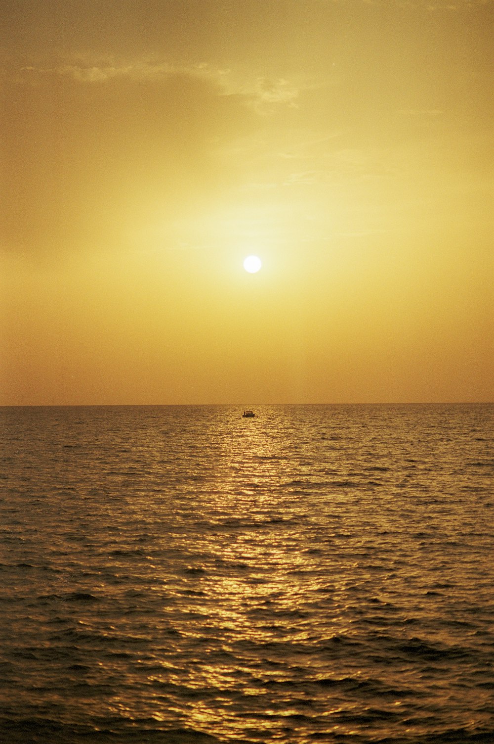El sol se está poniendo sobre el océano con un bote en la distancia