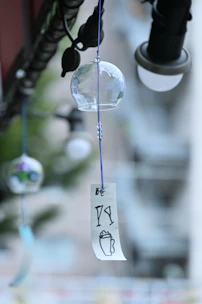 A delicate glass wind chime catching the light with its colorful beads hanging from a rustic wooden porch.