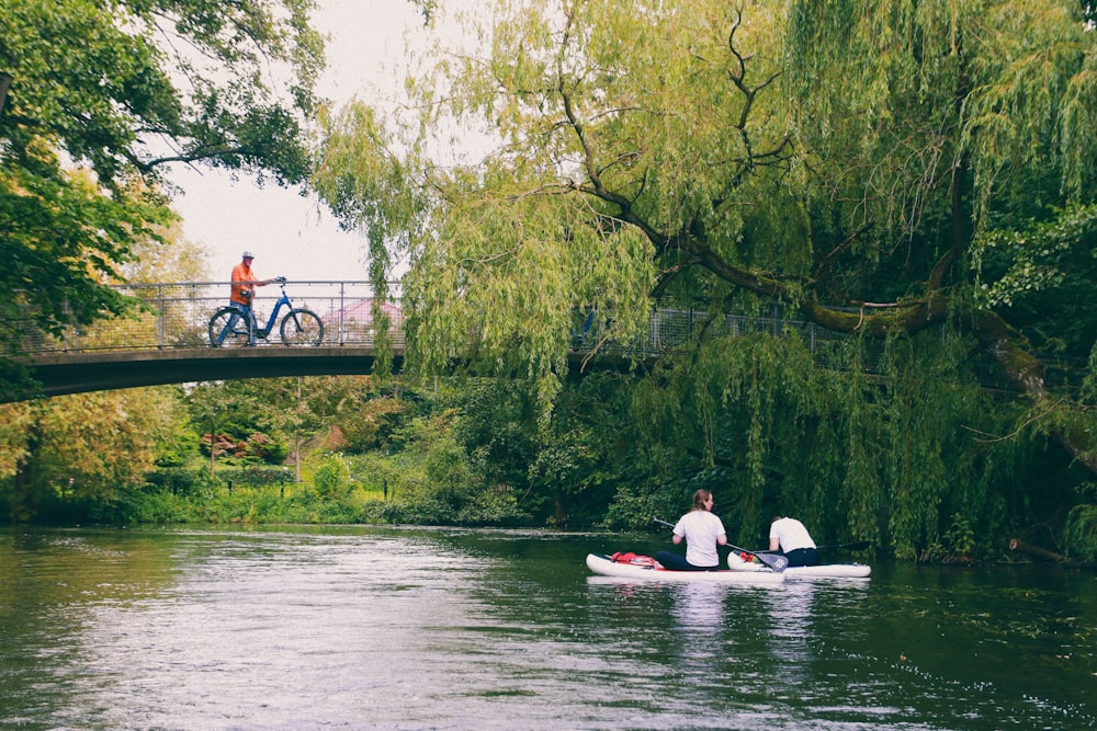 two people in a canoe on a river under a bridge