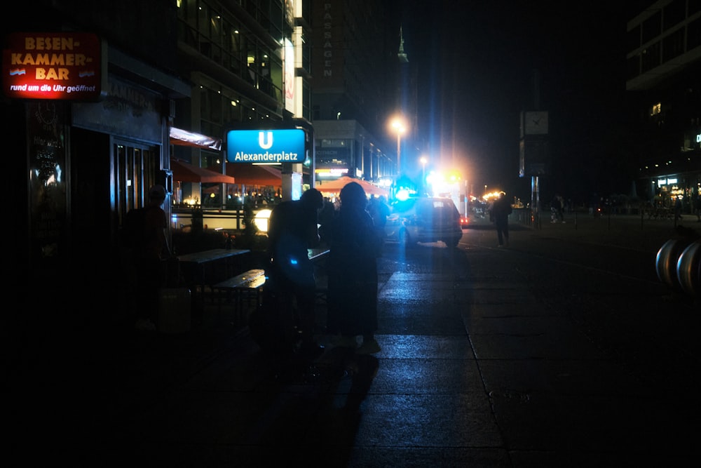 a couple of people standing on a sidewalk at night