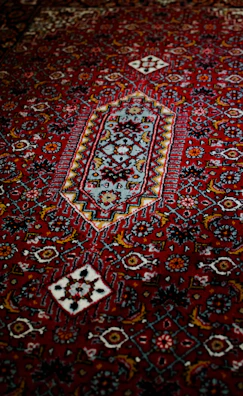 Close-up of a deep red Persian carpet with intricate gold and ivory floral patterns.