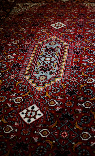 A close-up of a luxurious deep red Persian carpet with intricate gold and ivory floral patterns.