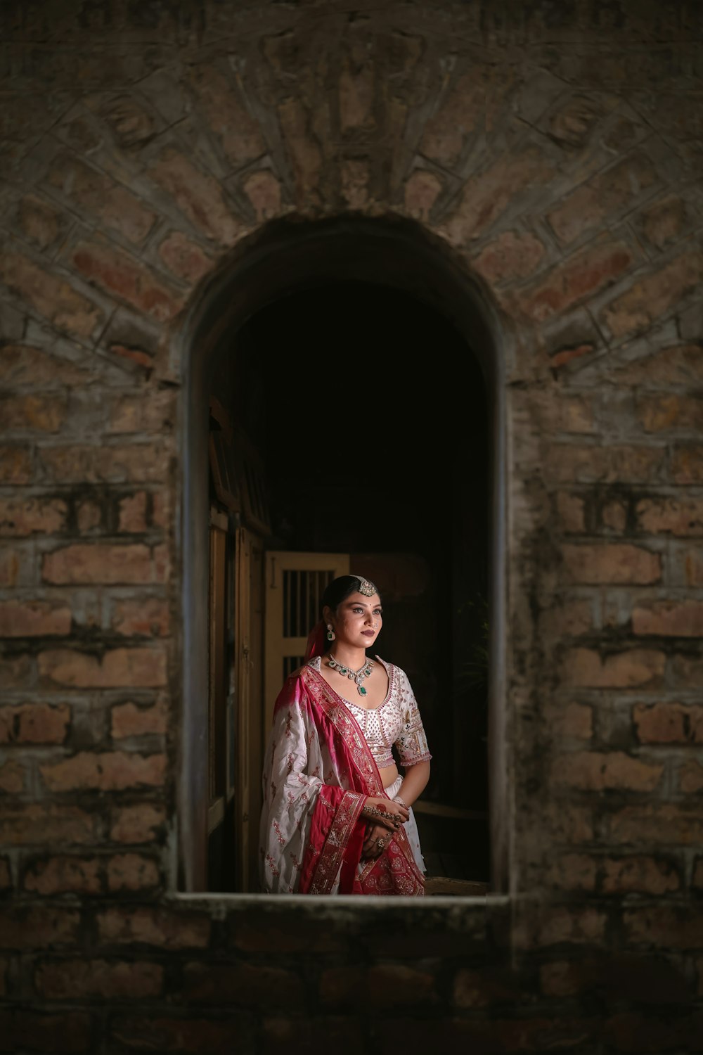 Una donna in un sari rosso e bianco che guarda fuori da una finestra