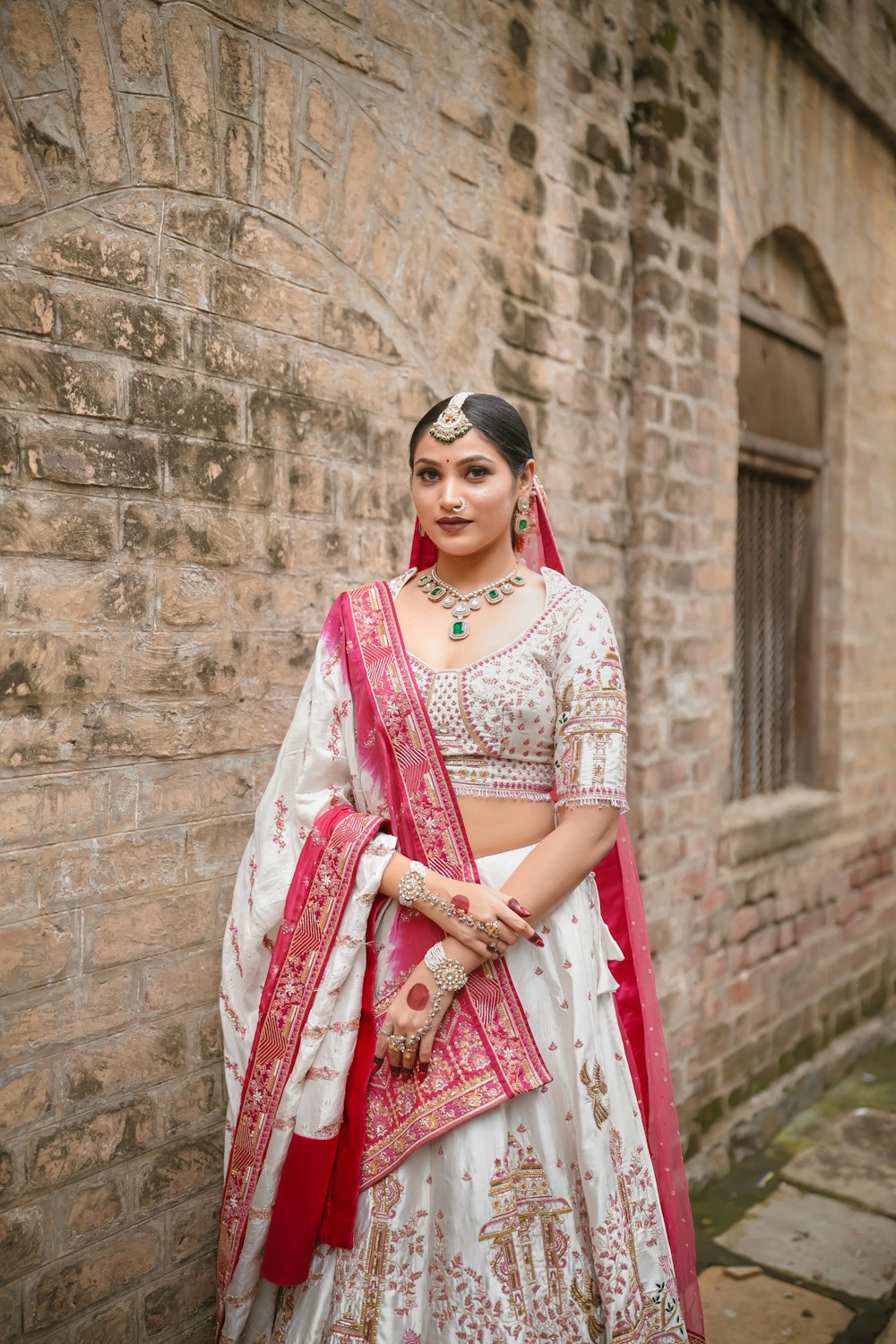 a woman in a white and red lehenga standing in front of a brick
