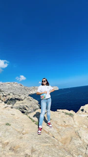 Adventure seeker perched on a rocky cliff edge, gazing into the horizon wearing Wild’s signature sunglasses against a crisp, clear sky.