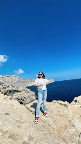 Adventure seeker perched on a rocky cliff edge, gazing into the horizon wearing Wild’s signature sunglasses against a crisp, clear sky.