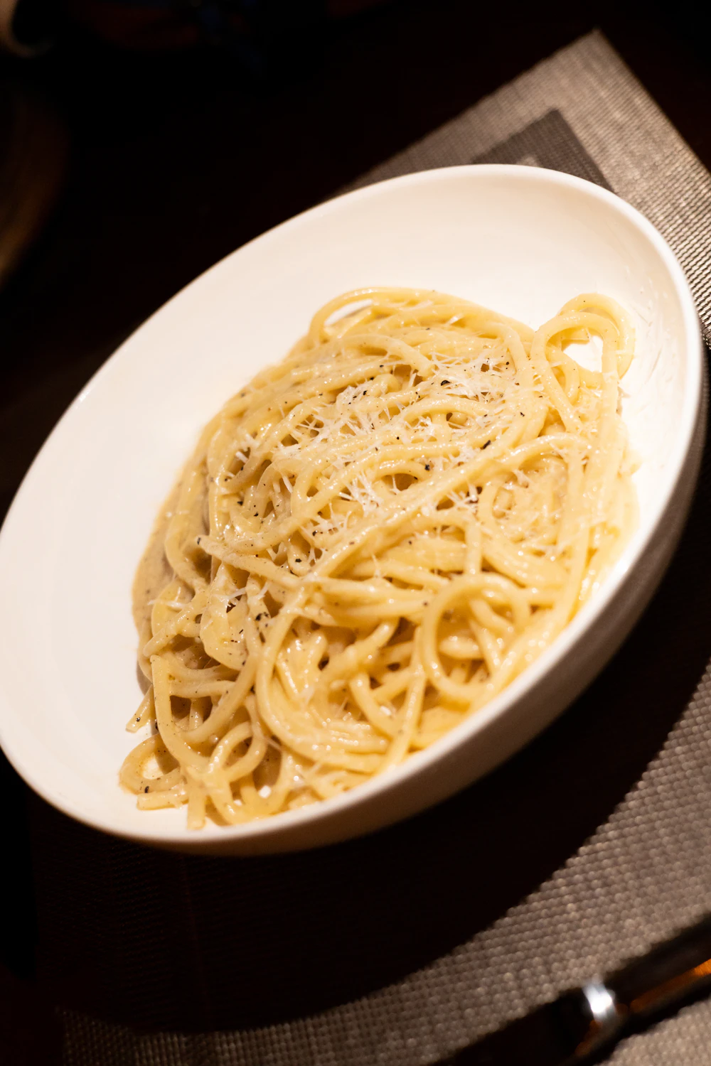 Spaghetti cacio e pepe cremosi in una ciotola bianca con pecorino e pepe macinato
