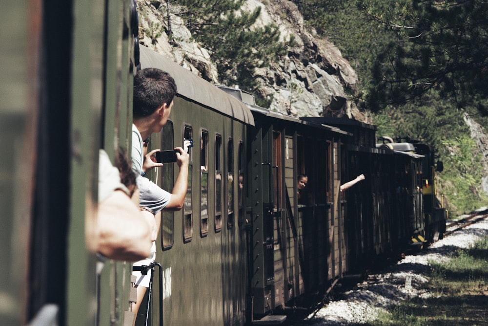 a man standing on the side of a train next to a forest