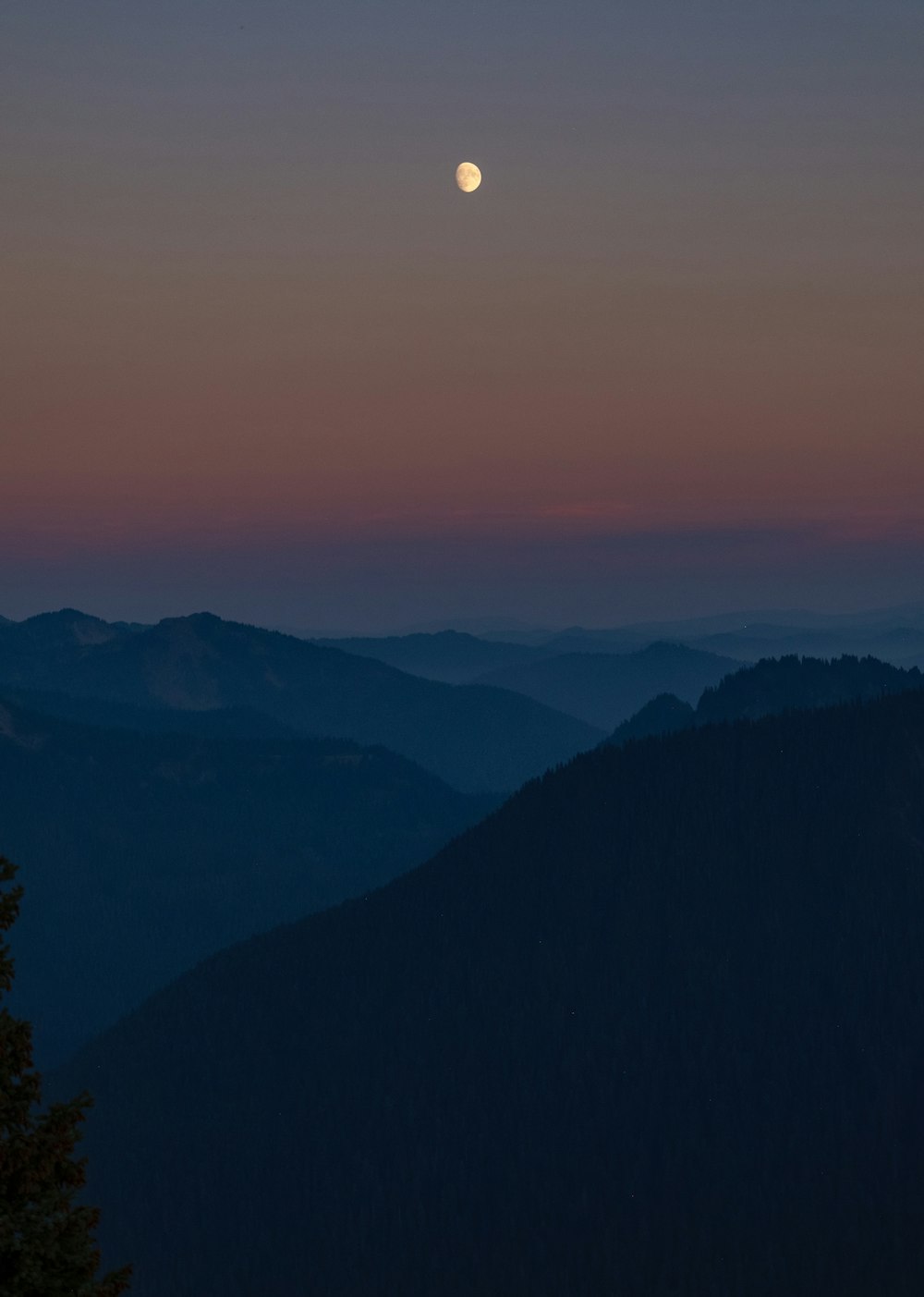 a full moon is seen over a mountain range