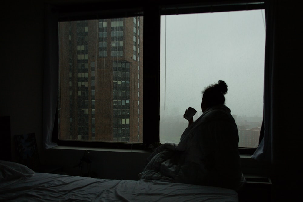 una persona seduta su un letto che guarda fuori da una finestra