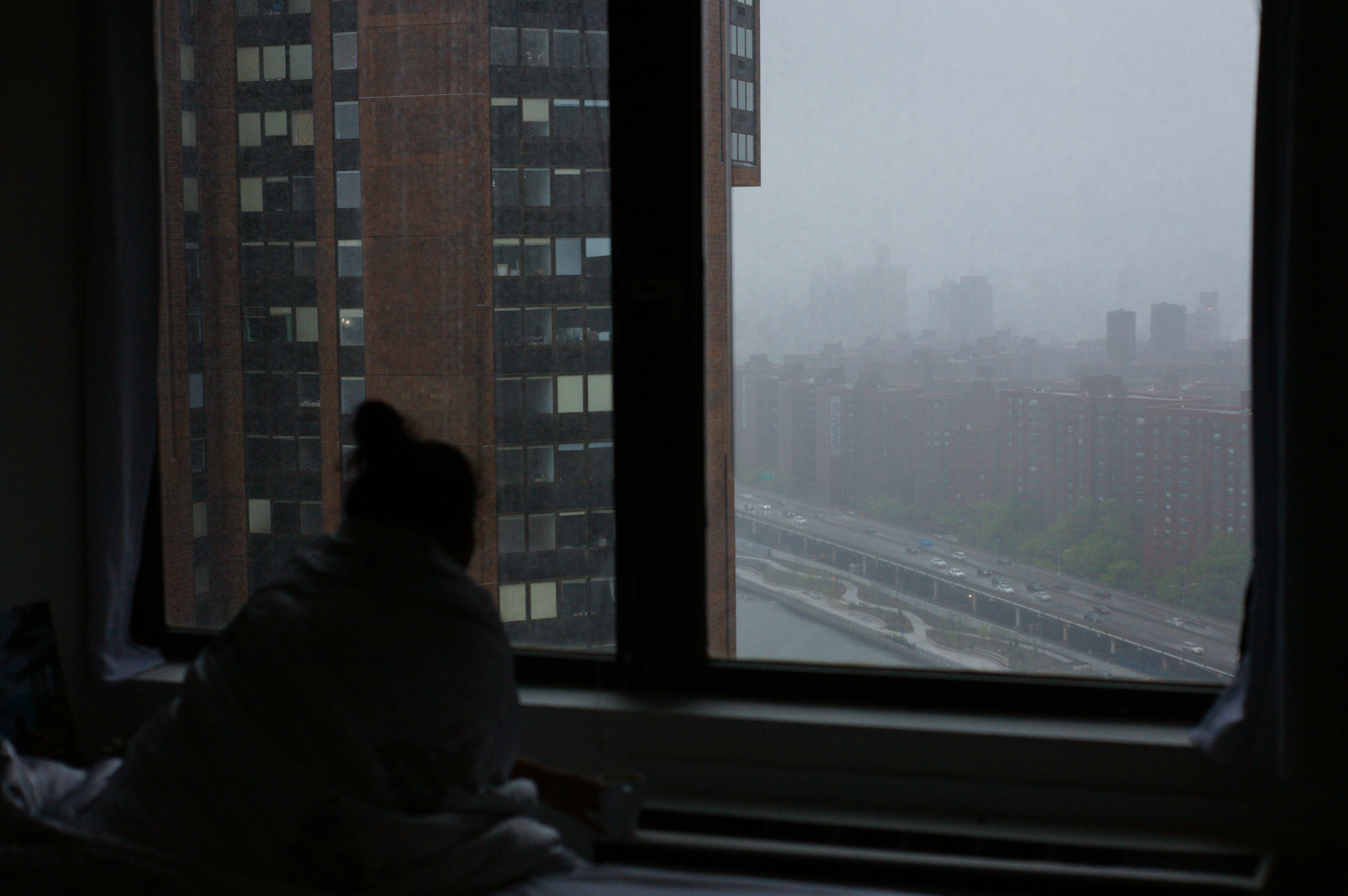 a person sitting on a bed looking out a window, 
