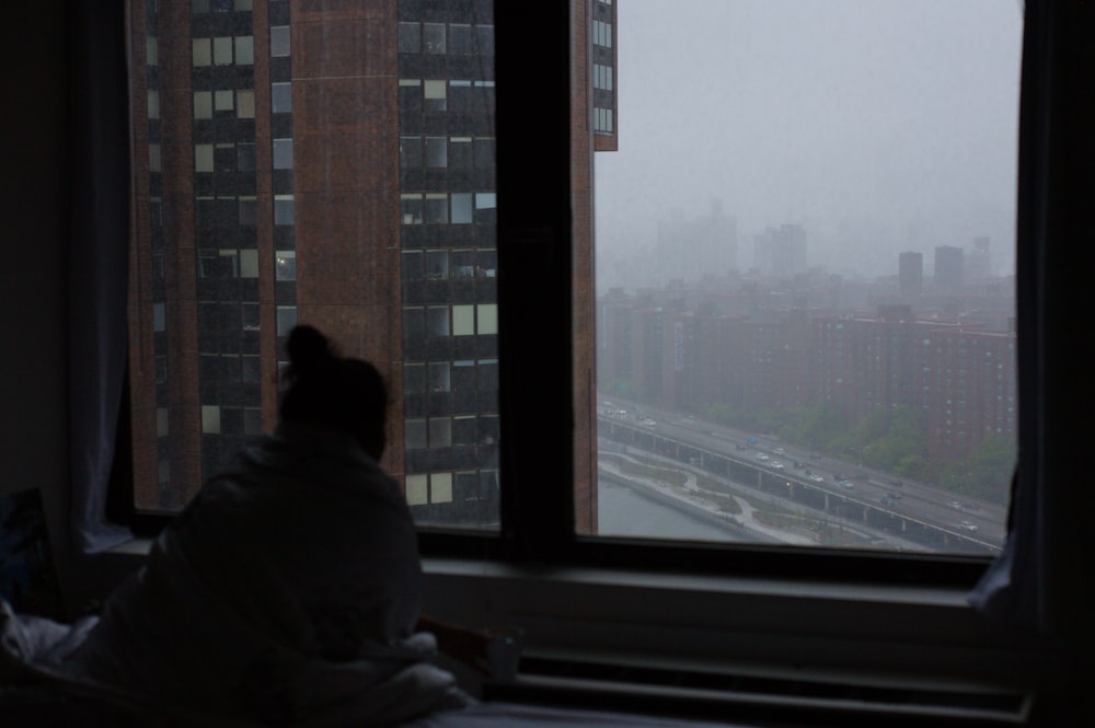 a person sitting on a bed looking out a window