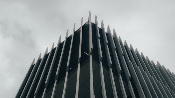 A modern building with a striking architectural design. Vertical metal or concrete fins protrude from the facade, creating an angular and geometric aesthetic. The overcast sky adds a moody and subdued background to the sharp, clean lines of the structure.