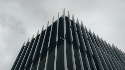 A modern building with a striking architectural design. Vertical metal or concrete fins protrude from the facade, creating an angular and geometric aesthetic. The overcast sky adds a moody and subdued background to the sharp, clean lines of the structure.
